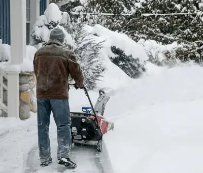 Residential snow removal technician using a snow blower to clear a home driveway and walkway in Spokane, WA